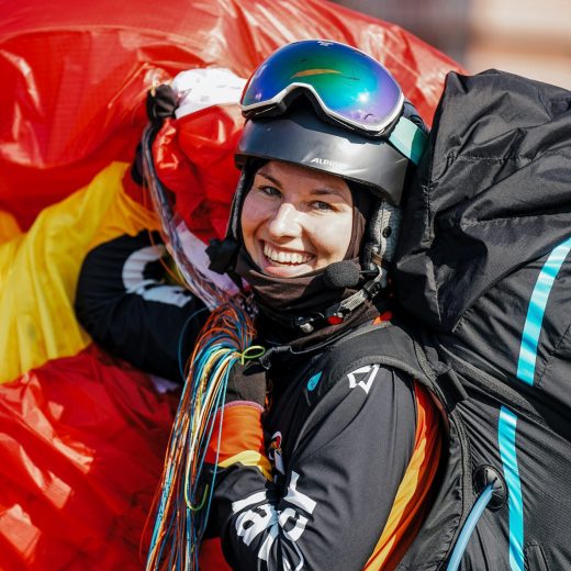 Julia Jauß Gleitschirm EM Serbien Julia Jauß in voller Gleitschirm Wettkampfausrüstung mit Schirm als Rosette über der Schulter lacht in die Kamera nach Landung auf der Gleitschirm Europameisterschaft in Serbien 2023