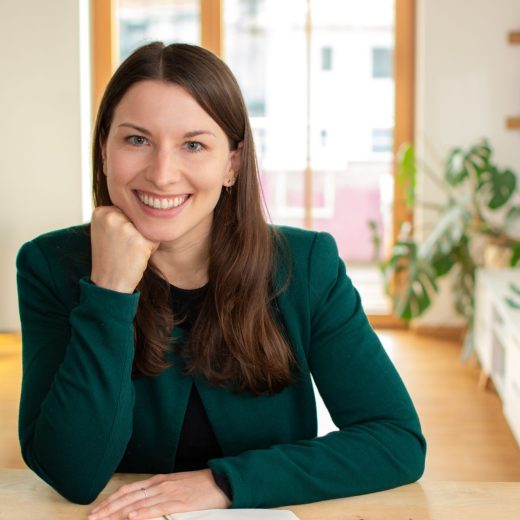 Favourit Julia Jauß entspannt lächelnd in die Kamera geschaut, Kopf auf der Faust abgestützt, freundliches Business-Porträt