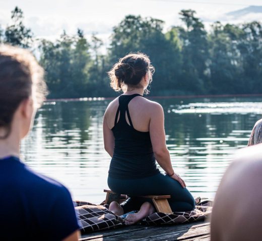 Julia Jauß von hinten mit einer Gruppe bei der Meditation am See in Greifenburg